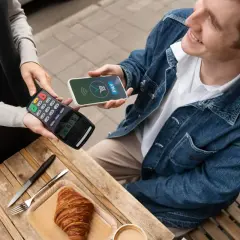 Uśmiechnięty mężczyzna płaci telefonem Santander za croissant. Szybko i wygodnie, jak płacić telefonem Santander.
