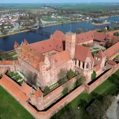 Malbork, największy zamek na świecie, z czerwonej cegły, otoczony murami obronnymi, nad rzeką Nogat.