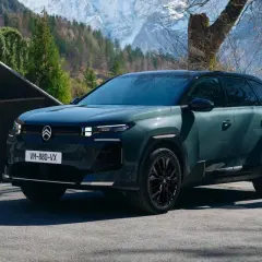 Nowy Citroën C5 Aircross 2025, zielony SUV, ładowany przy górskim domu. Kobieta w płaszczu wychodzi z budynku.
