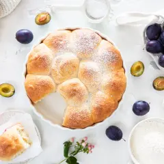 Ein goldbrauner Hefekuchen mit Puderzucker, umgeben von frischen Pflaumen. Perfekt für ein Buchty Rezept!