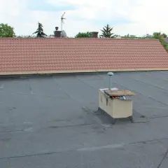 Płaski dach z papy, komin i fragment dachu skośnego z dachówką. To właśnie attyka co to za element?