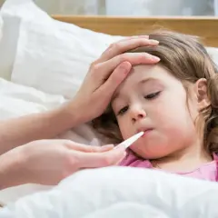Bambina a letto con termometro in bocca, mano sulla fronte. La febbre da ansia la fa stare male.