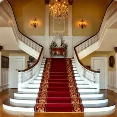 Elegancka, dwubiegowa klatka schodowa z czerwonym dywanem i żyrandolem.