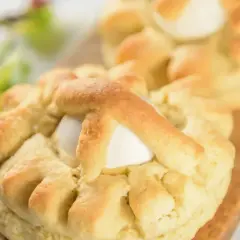 Dolci pasquali pugliesi con uova intere, decorati con impasto intrecciato, su un tagliere di legno.