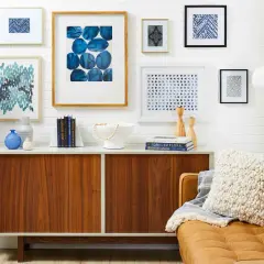 A stylish gallery wall features abstract blue art, geometric prints, and a framed textile.