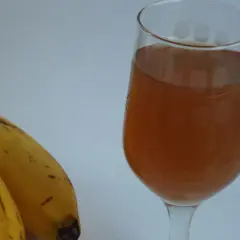 Dwa dojrzałe banany obok kieliszka z bursztynowym płynem, być może to domowe wino bananowe.