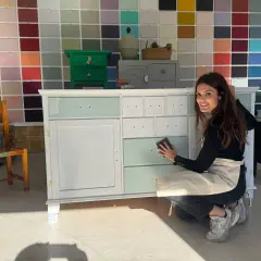 Mujer lijando un armario en proceso de pintura, con un fondo de muestras de colores.