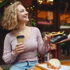 Uśmiechnięta kobieta z kawą płaci telefonem zbliżeniowo za croissant. Szybki przelew na telefon w kawiarni.