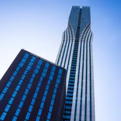 Två moderna skyskrapor mot en blå himmel. Den ena, med texten HOTEL KARLATORNET, har mörka fasader och blå fönster. Den andra är hög och smal med vita och blå vertikala linjer.