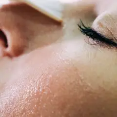 Gros plan sur une peau grêlée, humide et lumineuse, avec un œil fermé et des cils longs.