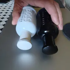 Dwie butelki perfum Hugo Boss, jedna biała męska, druga czarna, leżą obok siebie.