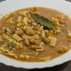 Un piatto fumante di pasta e fagioli, con pasta corta, fagioli borlotti, carote e una foglia di alloro.