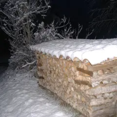 Une pile de bois peuplier chauffage sous la neige, prête pour l'hiver. Les branches enneigées d'un arbre se dressent à gauche.