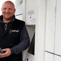 Uśmiechnięty kurier InPost trzyma skaner. Zastanawiasz się, ile zarabia kurier InPost?