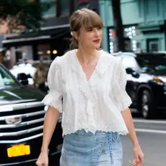 Chica con estilo "clean girl" con blusa blanca bordada y falda vaquera, paseando por la ciudad.