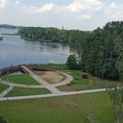 Malowniczy widok na jezioro i promenadę w Szczecinku. Widać ścieżki idealne na rowerowy spacer, mostek i zieleń.