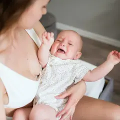Bambino piange per la dentizione neonato rimedi. Mamma lo culla, cercando sollievo.
