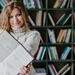 Kobieta z książką w bibliotece. Dowiedz się, jakie są zasady dystrybucji książek do bibliotek publicznych i szkolnych.
