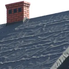 Ciemna papa bitumiczna na dachu, z widocznym fragmentem ceglanego komina.