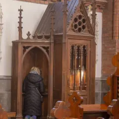 Kobieta klęczy w konfesjonale, szukając odpowiedzi na pytanie, czy antykoncepcja to grzech.