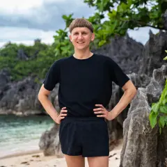 Pål Robinson står på en strand med klippor och grönska bakom sig.