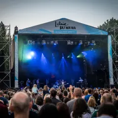 Koncert na Letnich Brzmieniach we Wrocławiu, scena z zespołem i tłum widzów.
