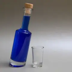 Niebieska wódka w butelce z korkiem i pusty kieliszek obok.