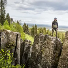 En man står på en klippa och njuter av utsikten över skog och landskap. En perfekt plats för att vandra i Europa.