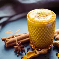 Ein Glas goldener Kurkuma Kaffee, verziert mit Zimtstangen, Sternanis und frischer Kurkuma.