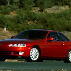 Czerwony Lexus SC400 na krętej drodze, otoczony zielonymi wzgórzami. Klasyczny sportowy samochód w ruchu.