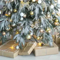 A frosted Christmas tree with gold and silver ornaments, fairy lights, and gifts wrapped in brown paper. Perfect christmas tree decor inspo for a cozy holiday.
