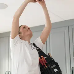 En elektriker med verktyg i bältet installerar en ojordad lampa i taket.