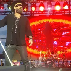 Koncert zespołu Perfect. Wokalista śpiewa, a na scenie widać gitarzystów i perkusję. Tło to czerwono-żółte wizualizacje. Autobiografia akordy.