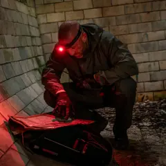 Mężczyzna w ciemnym ubraniu klęczy przy mapie, oświetlając ją czerwoną latarką czołową. Czerwone światło nie oślepia i nie zdradza pozycji.