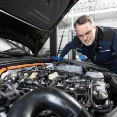Mecánico con gafas de seguridad revisa el motor de un coche para su mantenimiento anual.