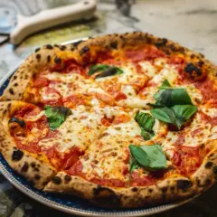 Pyszna pizza Margherita z bazylią na talerzu, obok nóż do pizzy.