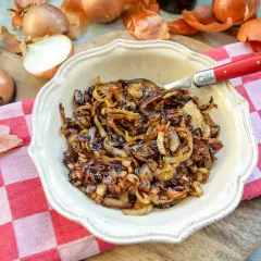 Eine Schüssel mit köstlichen, karamellisierten Zwiebeln, umgeben von frischen Zwiebeln und ihrer Schale. Perfekt als Beilage oder Topping.