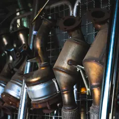 Varias partes del tubo de escape, incluyendo catalizadores y secciones de metal, cuelgan en un estante.
