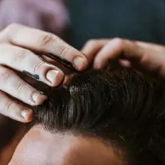 Main d'un coiffeur appliquant du gel ou de la cire sur les cheveux d'un client pour un coiffage parfait.