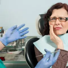 Kobieta z bólem zęba u dentysty. Lekarz w rękawiczkach pokazuje narzędzia, sugerując leczenie.