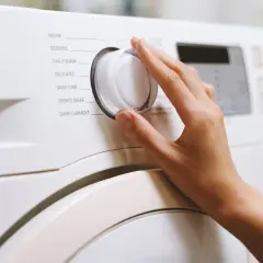 Dłoń kręci pokrętłem pralki, wybierając program "Bedding". Zastanawiasz się, w jakiej temperaturze prać pościel z kory? Sprawdź instrukcję pralki.