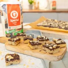 En saftig kanelbullekaka i långpanna, skuren i bitar och toppad med choklad och mandel. Perfekt för fikat!