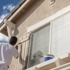 Pintor aplica pintura a persianas de ventana. ¿Cuál es la mejor pintura para fachadas? Busca durabilidad y resistencia a la intemperie.