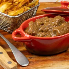 Un plat de carbonade flamande mijotée dans une cocotte rouge, accompagné de frites dorées dans un panier métallique. Un délice réconfortant.