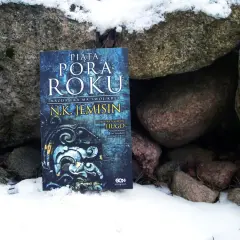 Książka "Piąta pora roku" N.K. Jemisin leży w śniegu między kamieniami. To opowieść o końcu świata, który przychodzi jak piąta pora roku.