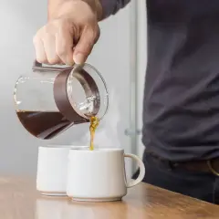Versando caffè da una caraffa in due tazze. La scelta del caffè giusto è fondamentale per una macchina caffè americano.