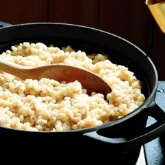 Un mestolo di legno affonda in una pentola piena di fumante orzo perlato, pronto per essere servito.