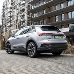Srebrny Audi Q4 elektryk z zieloną tablicą rejestracyjną stoi na brukowanym podjeździe przed nowoczesnym budynkiem mieszkalnym.