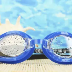 Niebieskie okulary do pływania męskie z kropelkami wody na soczewkach, na tle błękitnej wody i muszli. Gotowe na letnie przygody!