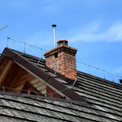 Dach z drewnianymi gontami, kominem i anteną. Widoczna instalacja odgromowa chroniąca budynek przed wyładowaniami atmosferycznymi.